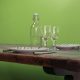 Une table rustique en bois pour deux personnes sur fond vert vif, idéale pour réfléchir à votre dernière création de site web. Elle comprend deux assiettes avec fourchettes assorties, des verres à vin vides et une bouteille d'eau à bouchon mécanique : idéale pour une discussion experte sur WordPress.