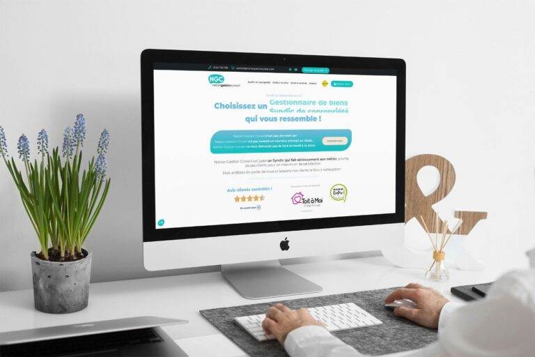 Une personne tape sur un clavier blanc à un bureau moderne avec un ordinateur affichant un site web de gestion immobilière français. Le bureau est agrémenté d'une plante en pot, d'une esperluette décorative, d'un carnet de notes et d'un stylo.