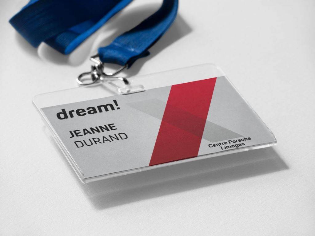 Un badge nominatif avec un cordon bleu affiche le texte dream !, JEANNE DURAND, et le Centre Porsche Limoges. Le motif comprend des formes diagonales rouges et grises sur fond blanc.